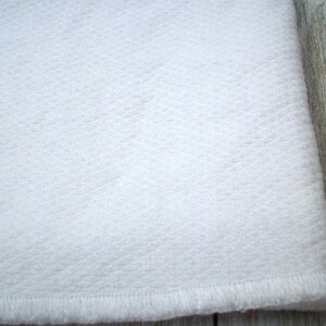 May include: White fabric with a textured surface and a stitched edge.