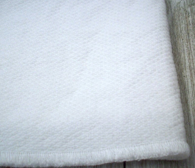 May include: White fabric with a textured surface and a stitched edge.
