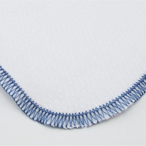May include: A white fabric square with a blue stitched border.