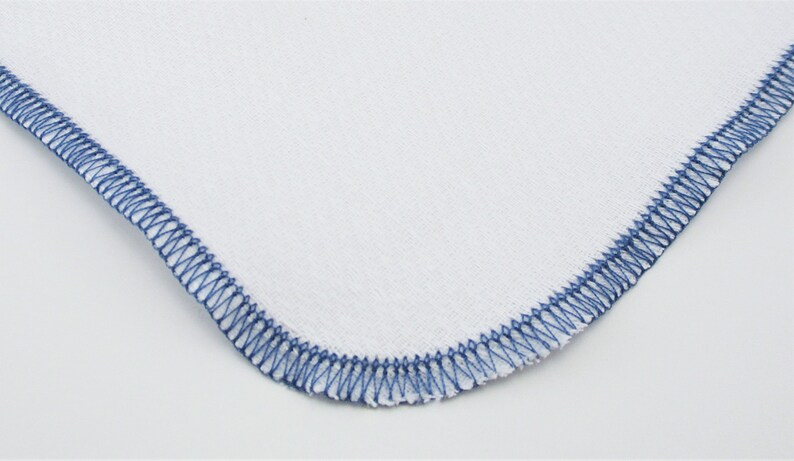 May include: A white fabric square with a blue stitched border.