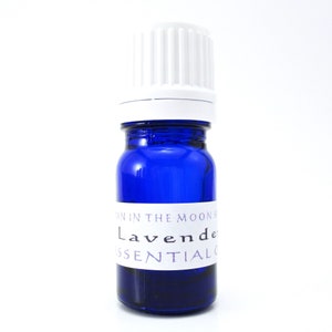 A cobalt blue glass bottle of Lavender essential oil. The shape of the bottle is squat and the cap is ribbed and white. It is labeled Man in the Moon Herbs Lavender Essential Oil.