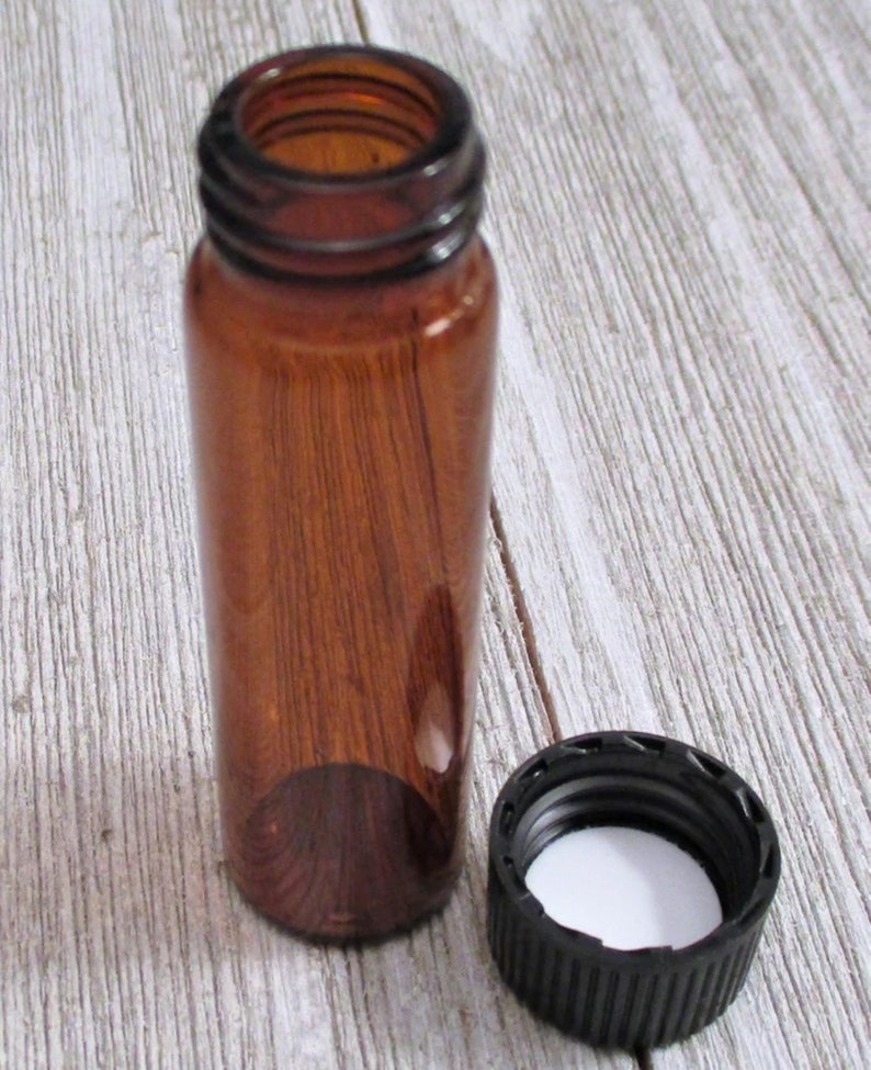 May include: A small amber glass bottle with a black screw-on lid. The bottle is empty and the lid is off.