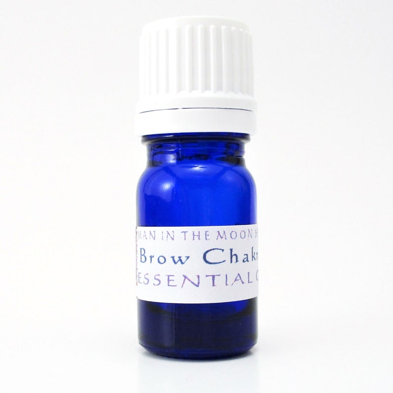 A blue glass bottle of Brow Chakra balancing oil. The shape of the bottle is squat and the cap is ribbed and white. It is labeled Brow Chakra essential oil and Man in the Moon Herbs.