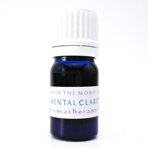A blue glass bottle of Mental Clarity essential oil blend. The shape of the bottle is squat and the cap is ribbed and white. It is labeled Man in the Moon Herbs Mental Clarity Aromatherapy Oil.