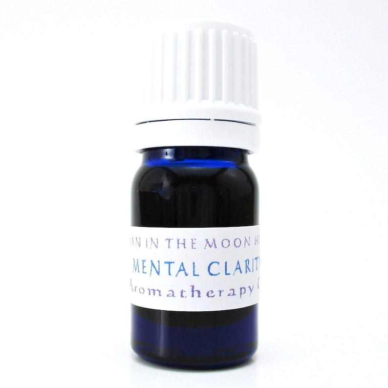 A blue glass bottle of Mental Clarity essential oil blend. The shape of the bottle is squat and the cap is ribbed and white. It is labeled Man in the Moon Herbs Mental Clarity Aromatherapy Oil.