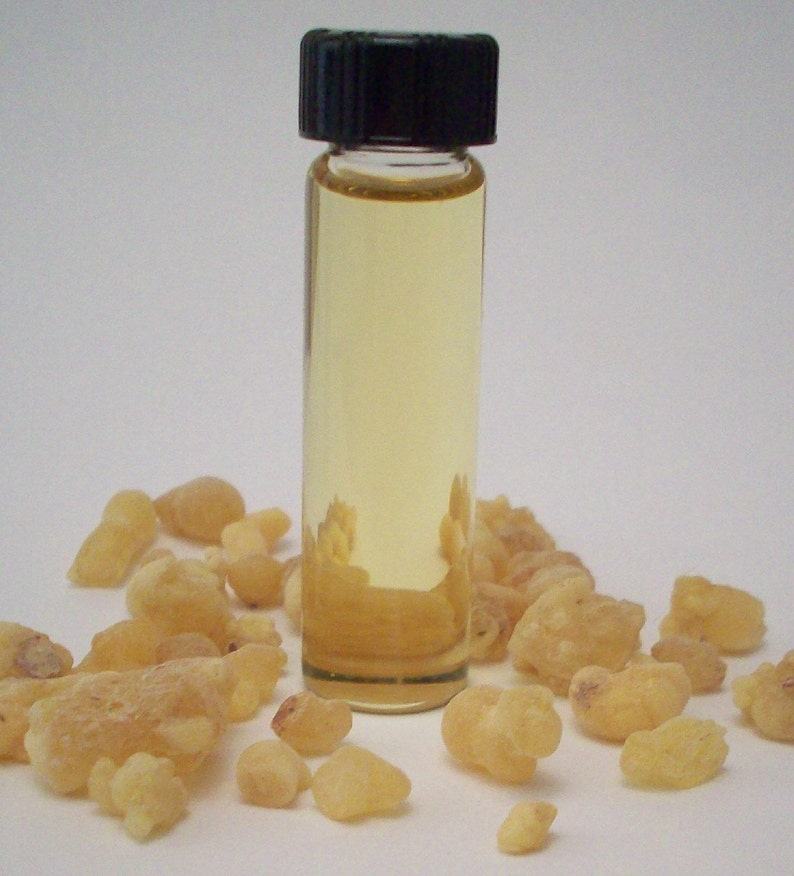 May include: A small glass bottle with a black cap filled with a light yellow liquid. The bottle is surrounded by small, irregularly shaped, light brown pieces of resin.