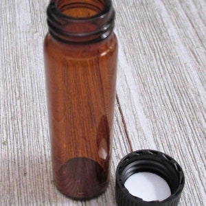 May include: A small amber glass bottle with a black screw-on lid. The bottle is empty and the lid is off.