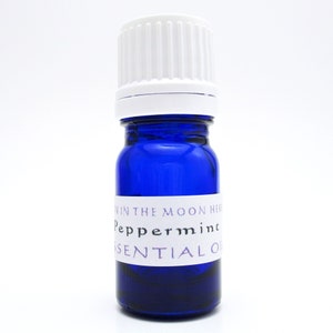 A cobalt blue glass bottle of Peppermint essential oil. The shape of the bottle is squat and the cap is ribbed and white. It is labeled Man in the Moon Herbs Peppermint Essential Oil.