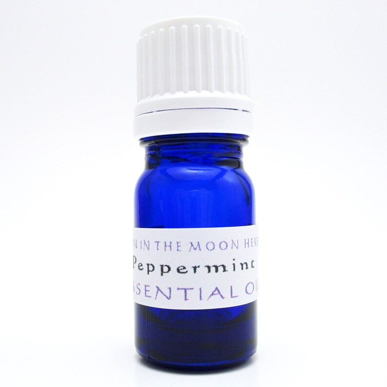 A cobalt blue glass bottle of Peppermint essential oil. The shape of the bottle is squat and the cap is ribbed and white. It is labeled Man in the Moon Herbs Peppermint Essential Oil.