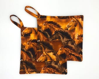 May include: Two square fabric pot holders featuring a repeating pattern of brown, black, and golden horses in motion. Each pot holder has a matching brown fabric loop attached to one corner for hanging, with a warm-toned, multi-horse print design.