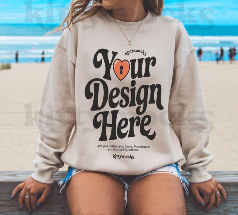 May include: A beige sweatshirt with a retro-style graphic that says "Your Design Here" with a heart and keyhole design. The text "kittymocks" appears above and below the graphic.