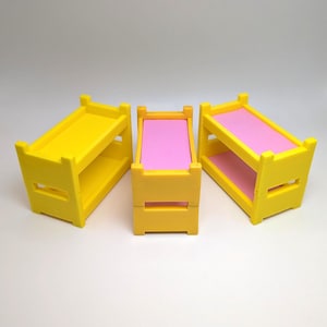 May include: Three yellow toy bunk beds with pink mattresses. The beds are made of plastic and are about 3 inches tall.