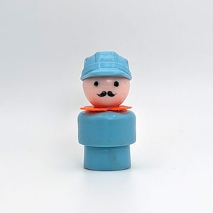 May include: A vintage Fisher-Price Little People figure. The figure has a light blue body and hat, a peach-colored head with a black mustache and eyes, and an orange collar. The toy is a classic collectible.