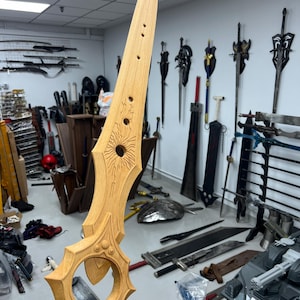 May include: A wooden sword with intricate carvings and a circular design on the blade. The sword is held in a hand, with other swords and shields visible in the background.