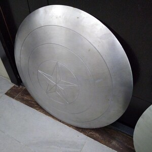 May include: A large, round, silver-colored metal shield with a five-pointed star in the center.