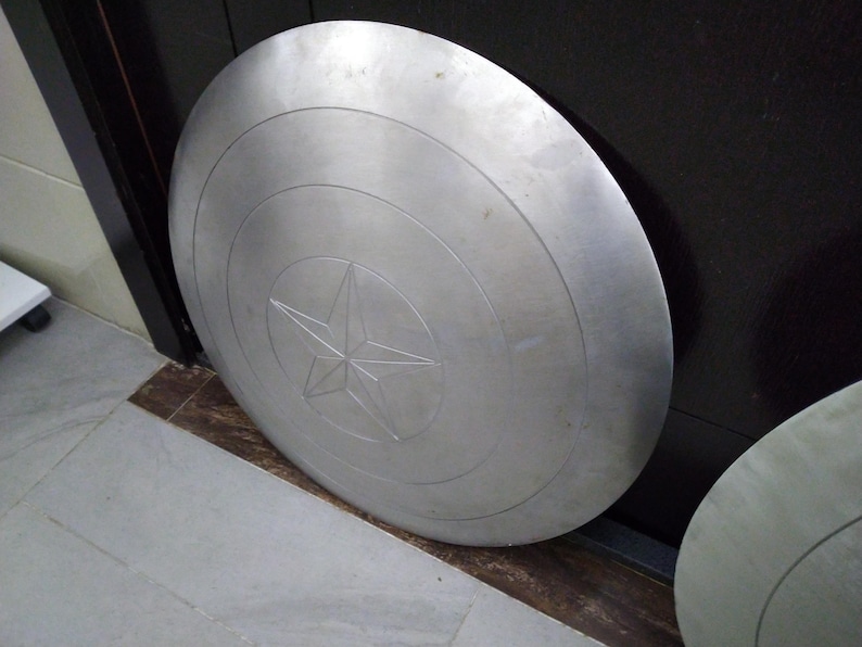 May include: A large, round, silver-colored metal shield with a five-pointed star in the center.