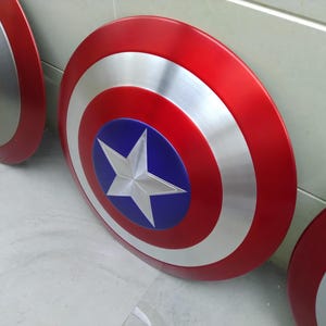 May include: Three Captain America shields, made of metal, with red, white, and blue paint. The shields are round and have a star in the center.