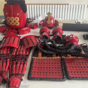 May include: A set of red and black samurai armor, including a helmet, chest plate, shoulder pads, and leg guards. The armor is decorated with gold accents and the number "888".