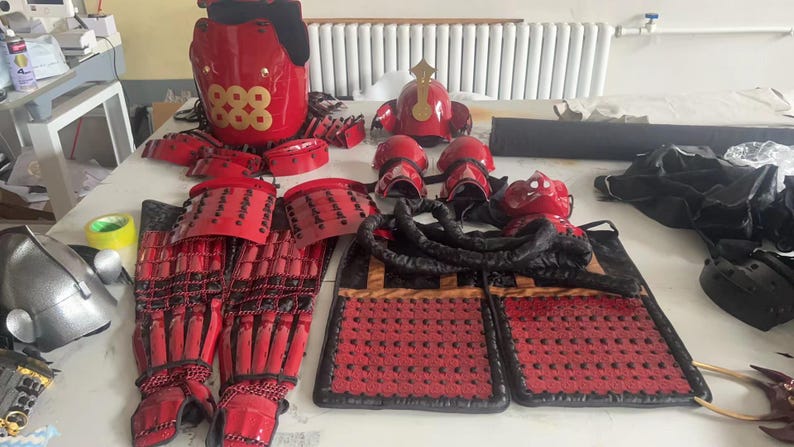 May include: A set of red and black samurai armor, including a helmet, chest plate, shoulder pads, and leg guards. The armor is decorated with gold accents and the number "888".