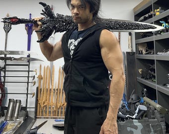 May include: A person holding a large, black, detailed sword with a red gem at the hilt. The sword is held horizontally across the person's body. The person is wearing a black sleeveless shirt and black pants. The background shows a room with shelves of swords and other items.