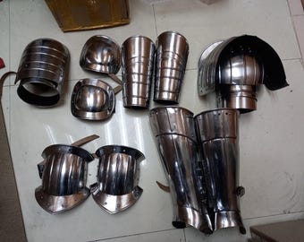 May include: A set of medieval-style armor pieces, including shin guards, knee pads, elbow pads, and arm guards. The armor is made of metal and has a silver finish.
