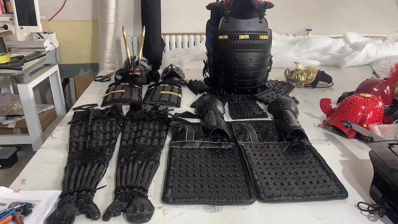 May include: A set of black samurai armor, including a helmet, chest plate, arm guards, and leg guards. The armor is made of a textured material and has a traditional Japanese design.