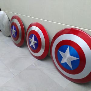 May include: Four Captain America shields, three red, white, and blue with a silver star, and one silver with a silver star. The shields are lined up on a white tiled floor.