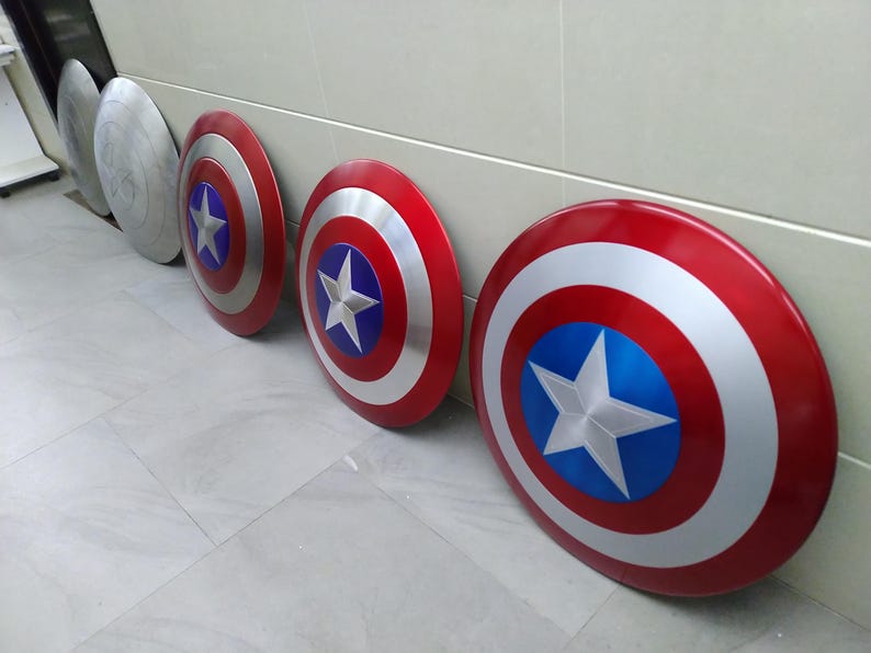 May include: Four Captain America shields, three red, white, and blue with a silver star, and one silver with a silver star. The shields are lined up on a white tiled floor.