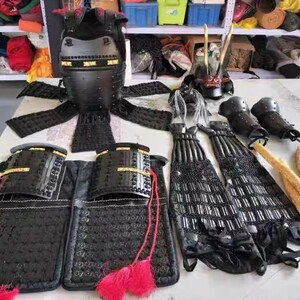 May include: A black samurai armor set with a helmet, chest plate, arm guards, and leg guards. The armor is made of metal and has a traditional Japanese design.