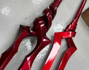 May include: Two red metal swords with intricate designs. The swords have a shiny, polished finish and are displayed on a white surface.