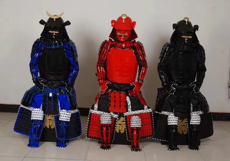 May include: Three samurai armor figures, one in red, one in blue, and one in black. Each figure is wearing a helmet and armor with intricate details. The figures are standing on a white surface.
