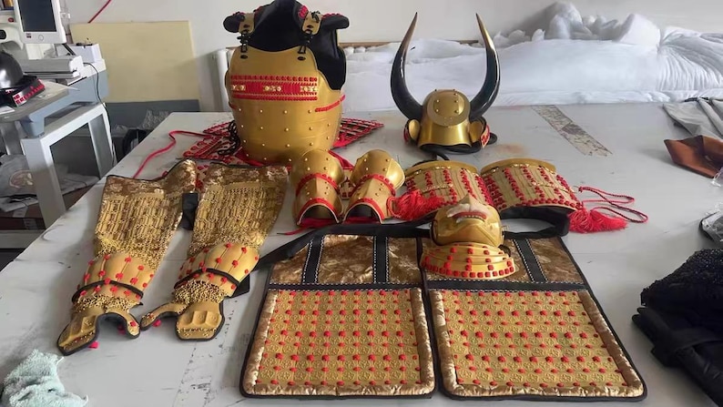 May include: A set of gold samurai armor with red accents. The armor includes a helmet, breastplate, gauntlets, and leg guards. The armor is decorated with small, red dots.