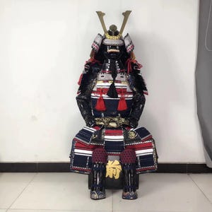 May include: A black and blue samurai armor with red accents. The armor is made of metal and fabric and is decorated with gold accents. The armor is sitting on a wooden stand.