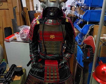 以下が含まれることがあります： 黒と赤のフルボディの侍の鎧。鎧は角と三日月模様のヘルメットを備えています。鎧は金属製で、複雑なディテールが施されています。