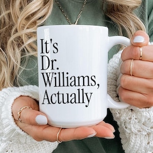 Könnte beinhalten: Eine weiße Keramiktasse mit schwarzem Text, der "It's Dr. Williams, Actually" lautet.