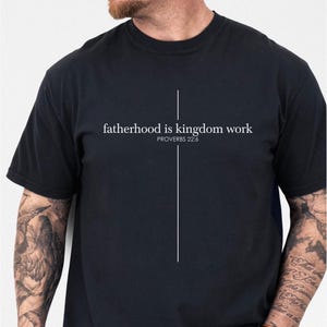 May include: Black t-shirt with the text "fatherhood is kingdom work" and the Bible verse Proverbs 22:6 in white. A vertical white line extends from the text. The word "BLACK" is printed at the bottom right.