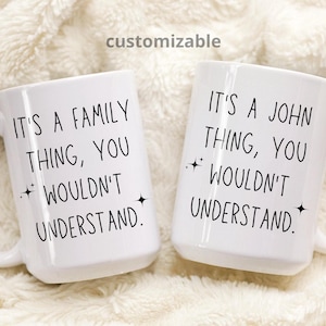 Puede incluir: Dos tazas de cerámica blanca con texto negro. La taza de la izquierda dice "Es una cosa de familia, no lo entenderías." La taza de la derecha dice "Es una cosa de John, no lo entenderías."