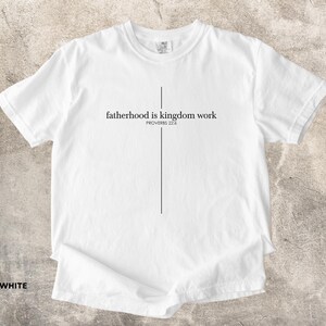 May include: White t-shirt with the text "fatherhood is kingdom work" in black, with a vertical line forming a cross. The text "PROVERBS 22:6" is below the main text. The word "WHITE" is at the bottom left.