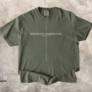 May include: Moss green t-shirt with the text "fatherhood is kingdom work" and the Bible verse Proverbs 22:6 in white. The shirt has a crew neck and short sleeves.