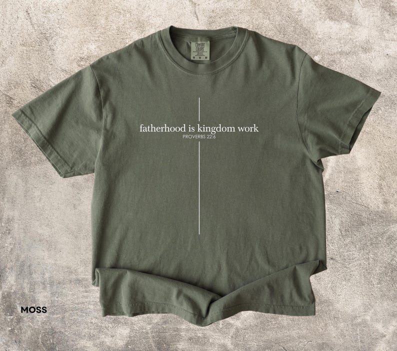 May include: Moss green t-shirt with the text "fatherhood is kingdom work" and the Bible verse Proverbs 22:6 in white. The shirt has a crew neck and short sleeves.