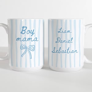Puede incluir: Dos tazas de cerámica blancas con rayas verticales azules. Una taza tiene el texto "Boy mama" y un lazo. La otra taza tiene los nombres "Liam Daniel Sebastian" en escritura azul. Ambas tazas tienen un asa blanca.