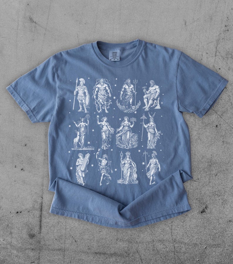 May include: A blue t-shirt featuring a white graphic of various Greek gods and goddesses. The figures are depicted in a classical style, with detailed illustrations. The shirt is made of a soft material and has a crew neck.