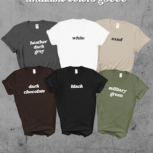 May include: A collection of six t-shirts in various colors: heather dark grey, white, sand, dark chocolate, black, and military green. Each shirt displays its color name in a simple, white font.