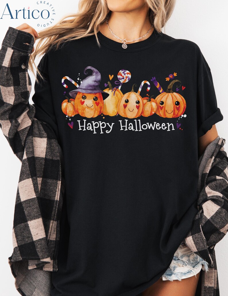 May include: Black t-shirt with a Halloween-themed graphic. The design features smiling orange pumpkins wearing a witch hat and holding candy canes, with the words "Happy Halloween" in white.