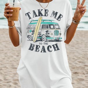 May include: White t-shirt with a graphic of a vintage surf van, a surfboard, and the text "TAKE ME TO THE BEACH" in black. The van is teal and white with palm trees and the word "SURF".