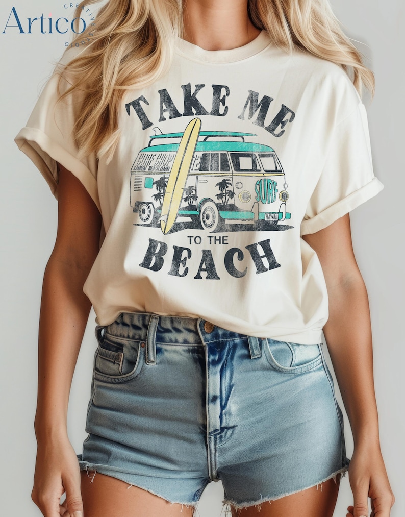 May include: Cream-colored t-shirt with a retro surf design. The graphic features a vintage van with a surfboard, palm trees, and the words "TAKE ME TO THE BEACH" in black. The shirt has rolled-up sleeves.