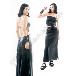 May include: Two women wearing black leather dresses. The dress on the left has a low back and is sleeveless. The dress on the right has a halter top and a skirt with a slight flare.