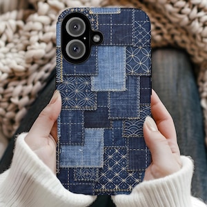 May include: A smartphone case with a patchwork denim design. The case features various shades of blue denim squares stitched together with gold thread. The design includes geometric patterns and a dual-lens camera cutout.