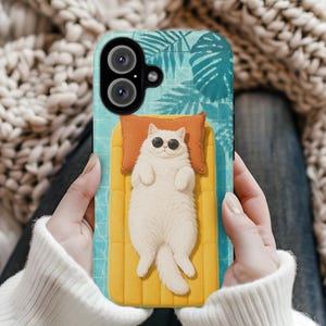 May include: A phone case featuring a white cat wearing black sunglasses, lying on a yellow inflatable pool float with an orange pillow. The background shows a blue swimming pool with palm leaf shadows and a camera lens cutout at the top.
