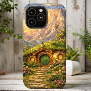 May include: A phone case featuring a colorful illustration of a hobbit hole nestled in a green hillside. The design includes a round green door, stone steps, and a mountain backdrop. The case has a glossy finish.